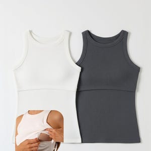 Könnte beinhalten: Zwei ärmellose Still-Tops. Eines ist weiß, das andere dunkelgrau. Beide haben eine gerippte Textur und ein integriertes Still-Panel. Das weiße Top wird im Bild vorgeführt.