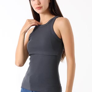K&ouml;nnte beinhalten: Ein dunkelgraues geripptes Tanktop mit rundem Ausschnitt und einem geschichteten Design. Das Oberteil besteht aus einem weichen, dehnbaren Material. Das Model tr&auml;gt blaue Jeans.