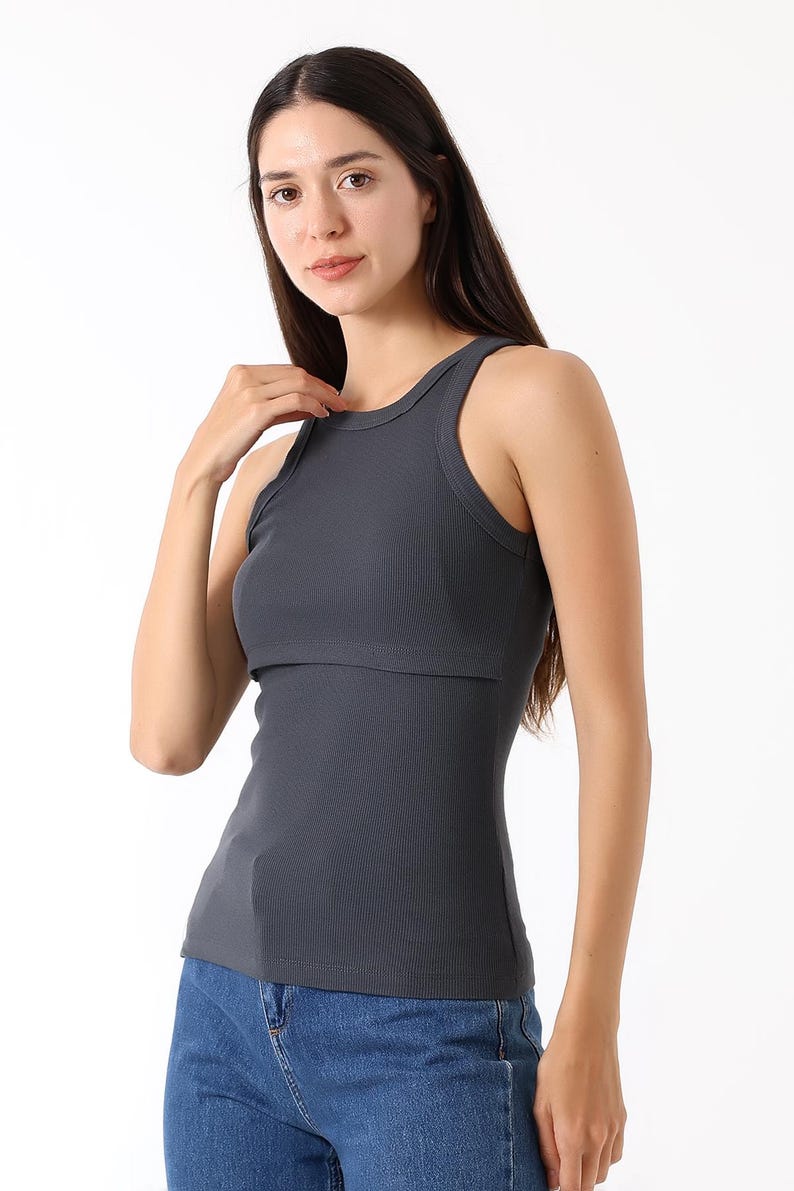 K&ouml;nnte beinhalten: Ein dunkelgraues geripptes Tanktop mit rundem Ausschnitt und einem geschichteten Design. Das Oberteil besteht aus einem weichen, dehnbaren Material. Das Model tr&auml;gt blaue Jeans.