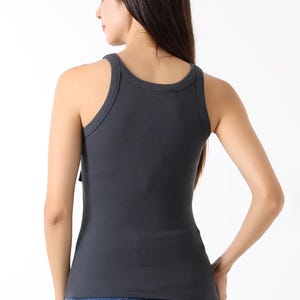 K&ouml;nnte beinhalten: Dunkelgraues geripptes Tanktop mit Rundhalsausschnitt und figurbetonter Silhouette. Das Tanktop wird mit blauen Jeans kombiniert. Das Model ist von hinten zu sehen, mit langen dunklen Haaren.