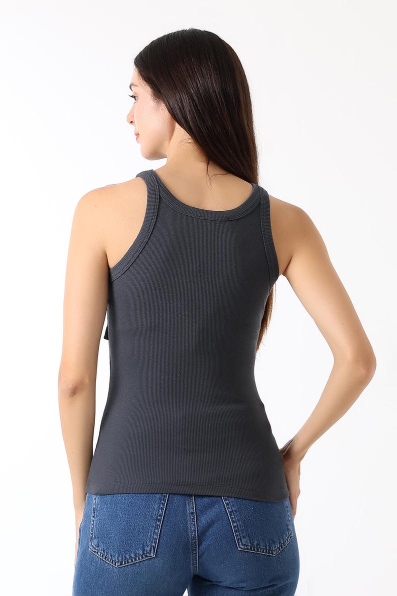 K&ouml;nnte beinhalten: Dunkelgraues geripptes Tanktop mit Rundhalsausschnitt und figurbetonter Silhouette. Das Tanktop wird mit blauen Jeans kombiniert. Das Model ist von hinten zu sehen, mit langen dunklen Haaren.