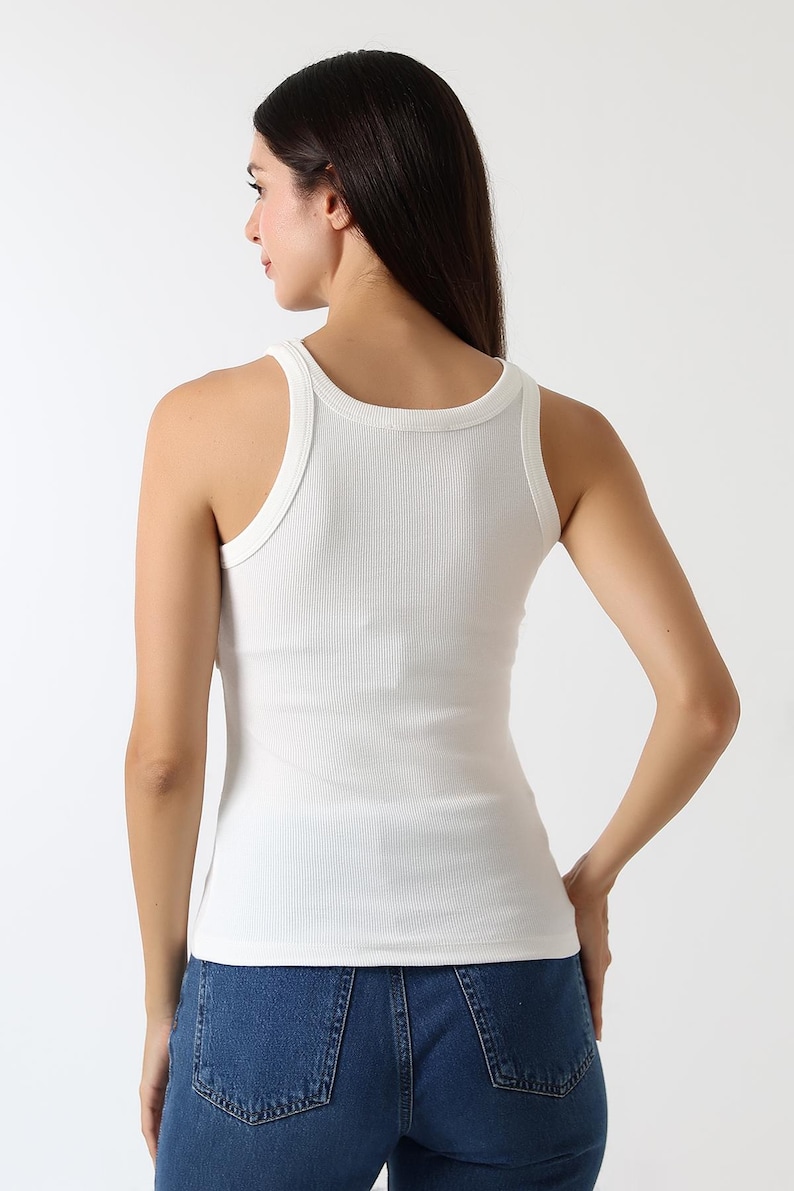 K&ouml;nnte beinhalten: Ein wei&szlig;es geripptes Tanktop mit Rundhalsausschnitt und breiten Tr&auml;gern. Das Tanktop wird mit blauen Jeans getragen. Das Model ist von hinten zu sehen.