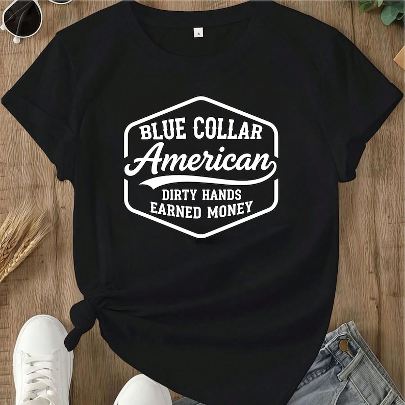 May include: Black t-shirt featuring the white text "BLUE COLLAR American DIRTY HANDS EARNED MONEY" in a shield design. The shirt has short sleeves and a crew neck. The shirt is knotted at the waist.