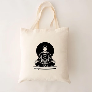 May include: Cream-colored tote bag featuring a black illustration of a meditating figure in a traditional Japanese outfit, with a katana sword below. The figure is set against a black circle, creating a minimalist design.