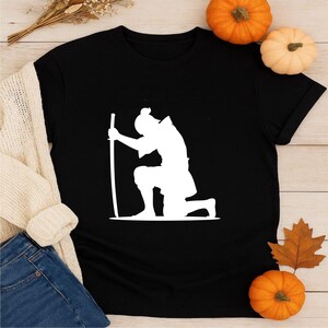 May include: Black t-shirt featuring a white silhouette of a kneeling samurai holding a sword. The design is a minimalist graphic, perfect for fans of Japanese culture and martial arts. The shirt is a classic crew neck.