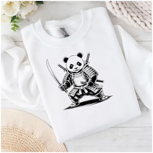 May include: White sweatshirt featuring a black and white illustration of a panda dressed as a samurai, holding two swords. The panda is wearing armor and has two additional swords on its back. The design is centered on the front of the sweatshirt.