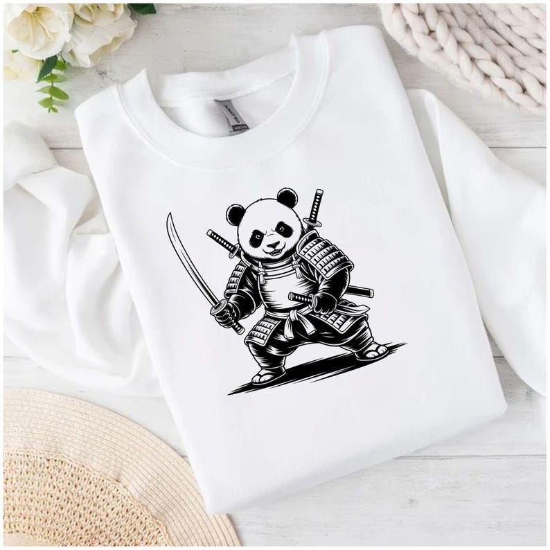 May include: White sweatshirt featuring a black and white illustration of a panda dressed as a samurai, holding two swords. The panda is wearing armor and has two additional swords on its back. The design is centered on the front of the sweatshirt.