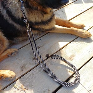 May include: A black and white twisted rope dog lead featuring silver-toned metal hardware, including a swivel snap hook at one end and multiple metal rings along the length of the rope for adjustable length and secure attachment points.