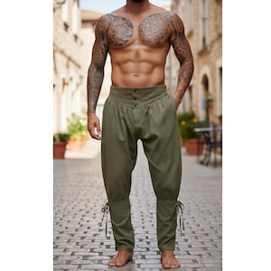 May include: Olive green pants with a high waist and button details. The pants have a loose fit through the legs, tapering to the ankles, and are secured with ties. The pants are made of a textured fabric.