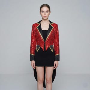 May include: A red sequined tailcoat with black lapels and gold trim. The jacket has long sleeves and a unique cut with a longer back. The garment is worn over a black dress.