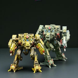 May include: Two detailed miniature mechs. One is predominantly yellow with red and clear accents, the other olive green. The mechs are posed on a black surface, highlighting their intricate designs and mechanical details. The image has an X-Art Studio logo.