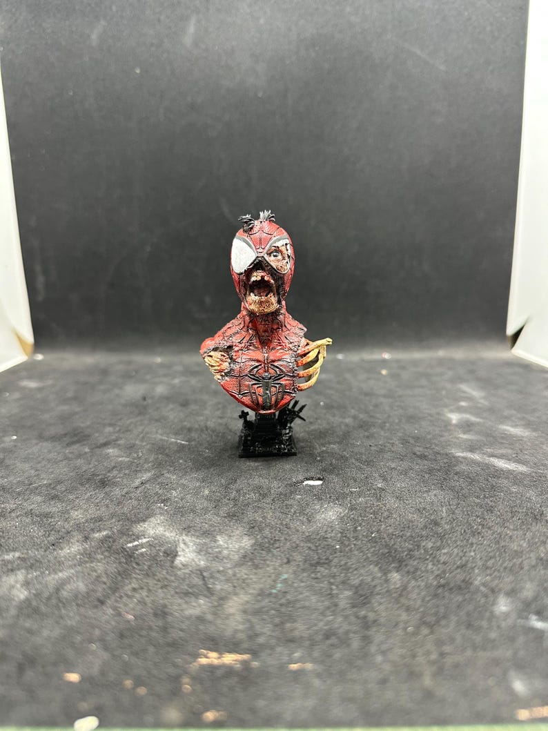 May include: A detailed bust of a zombie Spider-Man, featuring a red and black costume with exposed flesh and bone. The figure is mounted on a black base, showcasing intricate details and a distressed appearance. The bust is a collectible item.
