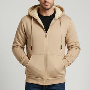 May include: A tan zip-up hoodie with a fleece-lined hood and pockets. The hoodie has a full-length zipper and drawstrings. The model is wearing a black t-shirt and blue jeans.