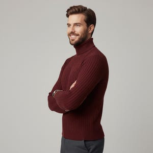 May include: A burgundy turtleneck sweater with a ribbed design. The sweater is made of a soft material and is worn with gray pants. The person is smiling with their arms crossed.