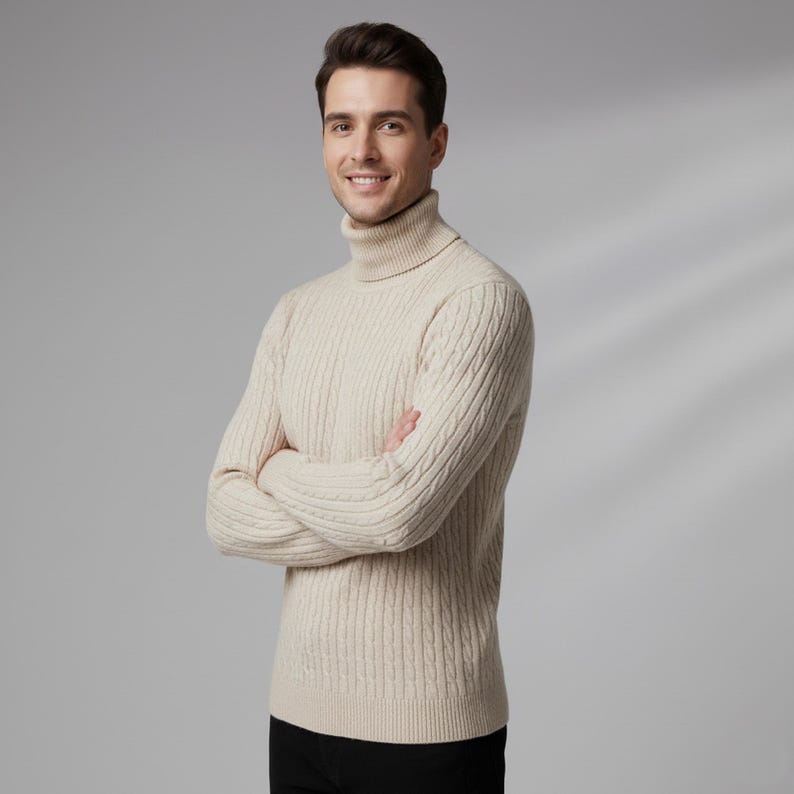 May include: A cream-colored cable-knit turtleneck sweater. The sweater has a ribbed texture and a high, folded collar. The person is wearing black pants. The person is smiling with their arms crossed.