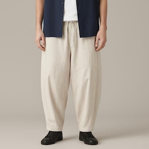 May include: Beige, loose-fitting pants with a drawstring waist and stitched panel details. The pants are paired with a navy blue button-down shirt and black shoes. The casual style is suitable for everyday wear.