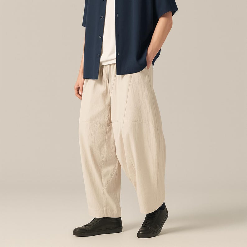 May include: Beige, wide-leg pants with a relaxed fit. The pants have a drawstring waist and are paired with a dark blue short-sleeve shirt and black sneakers. The outfit is casual and comfortable.