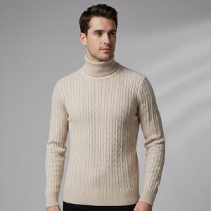May include: A beige turtleneck sweater with a cable knit design. The sweater has a ribbed collar and cuffs. The model is wearing a black bottom. The sweater is made of a soft, warm material.