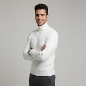 May include: A white cable-knit turtleneck sweater. The sweater has a ribbed hem and cuffs. The person is wearing a silver watch and gray pants. The background is a solid light gray.