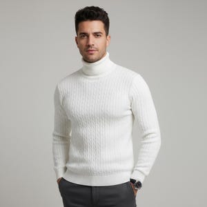 May include: A white cable-knit turtleneck sweater. The sweater has a ribbed texture and a high, folded collar. The sleeves are long, and the fit appears to be a classic style. The person is wearing a watch with a silver band and a dark face.