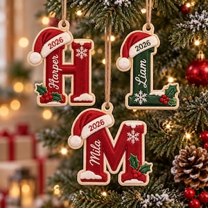 May include: Three hanging Christmas ornaments shaped as the letters H, L, and M. Each letter features a red Santa hat with the year 2026, a white snowflake, and holly berries. The letters are personalised with the names Harper, Liam, and Mila.