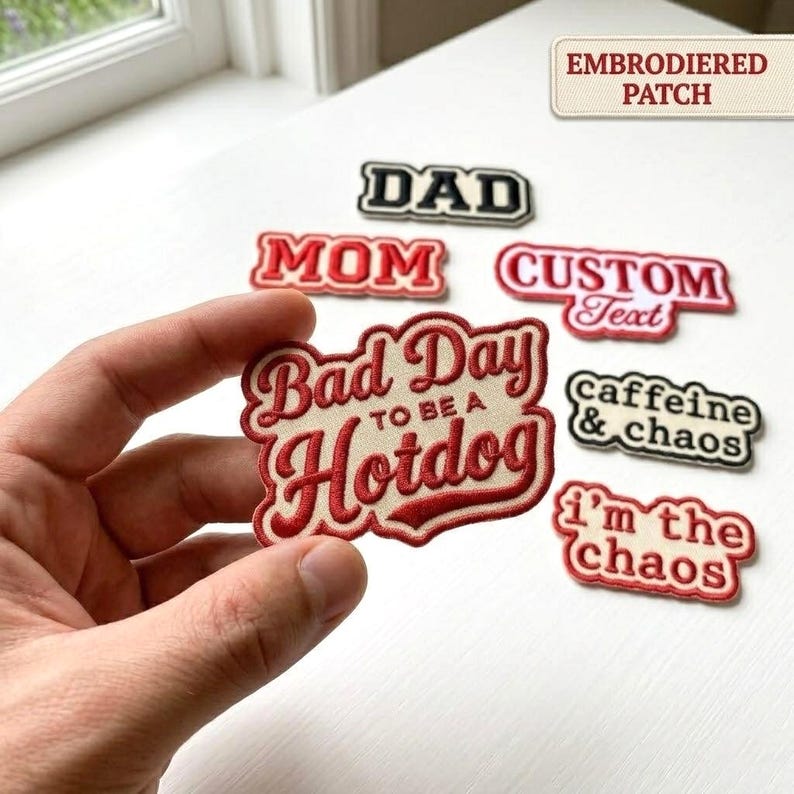 May include: Embroidered patches with various text designs, including "DAD," "MOM," "CUSTOM Text," "Bad Day to be a Hotdog," "caffeine & chaos," and "I'm the chaos." The patches are in red, black, and white.