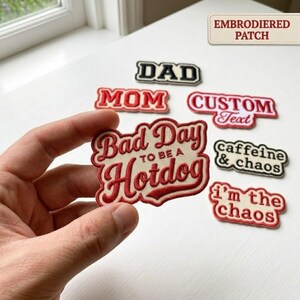 May include: A collection of embroidered patches with red and cream text. One patch held in the foreground reads 'Bad Day TO BE A Hotdog'. Other patches include 'DAD', 'MOM', 'CUSTOM Text', 'caffeine & chaos', and 'i'm the chaos' with a label reading 'EMBRODIERED PATCH'.