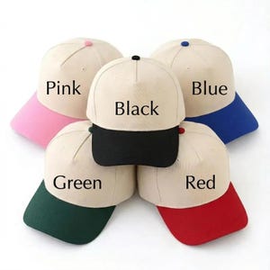 May include: A collection of baseball caps in various colors. Each cap has a beige crown and a colored brim. Colors include pink, blue, green, red, and black. The color of each brim is labeled in white text on the crown.