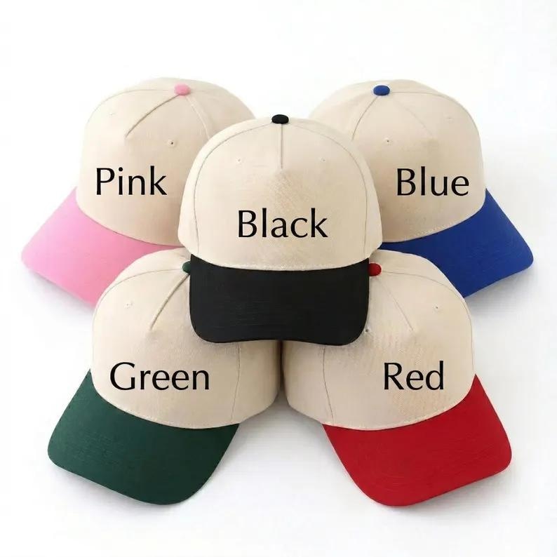 May include: Five baseball caps with beige crowns and colored brims. The caps feature text labels: Pink, Blue, Black, Green, and Red, corresponding to the brim colors. Each cap has a matching colored button on the top center of the crown.
