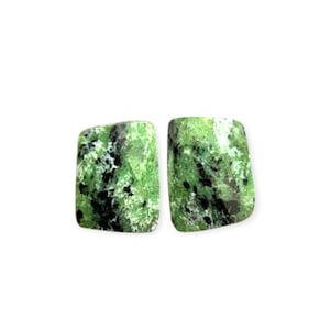 Könnte beinhalten: Zwei rechteckige Edelsteine mit einem lebendigen Grünton, gesprenkelt mit schwarzen Einschlüssen. Die polierten Steine haben eine glatte Oberfläche, ideal für die Schmuckherstellung oder das Sammeln. Die Edelsteine sind vor einem weißen Hintergrund platziert.