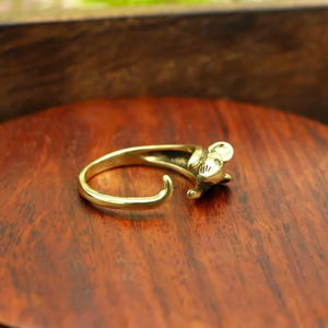 May include: A gold-colored ring in the shape of a mouse. The ring features a detailed mouse head and a curved band that wraps around the finger. The ring is made of a shiny, metallic material.