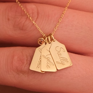 May include: A gold-colored necklace featuring three rectangular pendants, each engraved with a name: "Joanna", "Kylie", and "Sally". The pendants hang from a delicate chain, creating a personalized accessory.