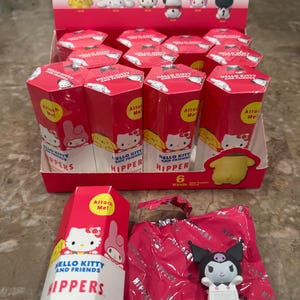 May include: A display of Hello Kitty and Friends "Hippers" decorative mini figures. The display includes red boxes with character illustrations and the text "Attach Me!". A Kuromi figure is visible on a pink wrapper.