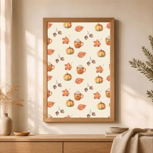 Könnte beinhalten: Ein rechteckiger Wandkunstdruck in einem hellen Holzrahmen mit einem sich wiederholenden Muster aus herbstlichen Aquarellmotiven, darunter orangefarbene Kürbisse, braune Eicheln, bunte Herbstblätter und Kaffeetassen mit Sahnehaube.