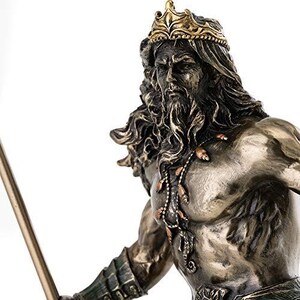 May include: A bronze-toned statue of a bearded man wearing a gold crown and a necklace. The statue has long, flowing hair and is holding a spear. The figure is muscular and detailed, with intricate carvings on the armor.