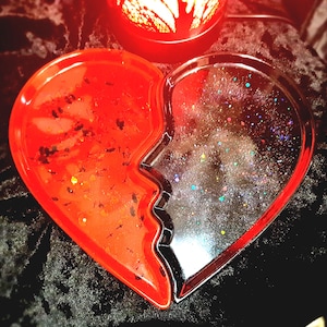 May include: A heart-shaped tray split in two, with a jagged edge. One side is red with black specks, the other is clear with colorful glitter. The tray is likely made of resin.