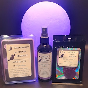 May include: A selection of Midnight Moon Market products, including wax melts, a fragrance spray, and moondust discs. Each item has a label with a crescent moon and cat logo. The products are dark, with a purple glowing orb in the background. The spray bottle is 100ml.