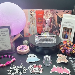 Puede incluir: Una colección de artículos con temática de Halloween, que incluye ceras perfumadas, pegatinas, una pulsera y arte de uñas. La imagen presenta una lámpara en forma de luna brillante, una pinza para el pelo transparente y varios elementos decorativos.