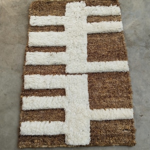 May include: A rectangular brown and white rug with a geometric design. The rug features a textured, woven appearance with a pattern of thick, white lines against a brown background. The design is symmetrical, creating a bold, graphic statement.