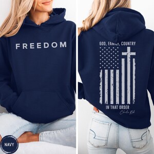 May include: Navy blue hoodie with the word "FREEDOM" printed in white on the front. The back features an American flag design with a cross and the text "GOD, FAMILY, COUNTRY IN THAT ORDER".
