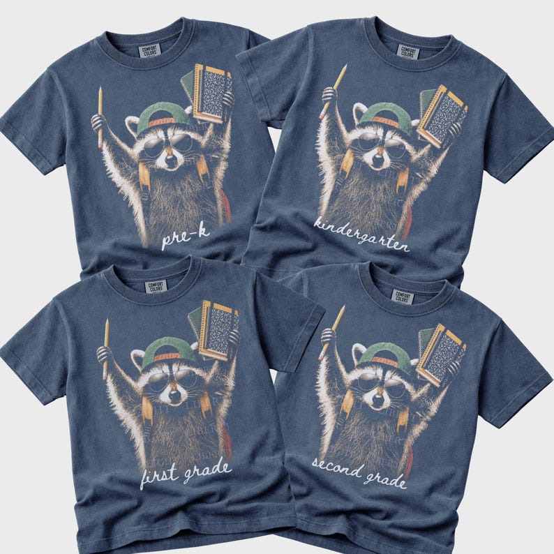 May include: Four blue short-sleeve t-shirts featuring a graphic of a raccoon wearing sunglasses and a green cap, holding a pencil and books. The shirts are labelled with the text pre-k, kindergarten, first grade, and second grade in white script.