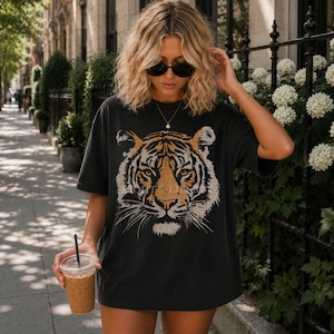May include: A charcoal grey short-sleeve t-shirt featuring a large, detailed graphic print of a tiger face in shades of orange, black, and white. The shirt has a crew neckline and a relaxed, oversized fit with a distressed, vintage-style aesthetic.
