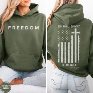 May include: Military green hoodie with the word "FREEDOM" printed in white on the front. The back features an American flag design with a cross and the text "GOD, FAMILY, COUNTRY IN THAT ORDER".