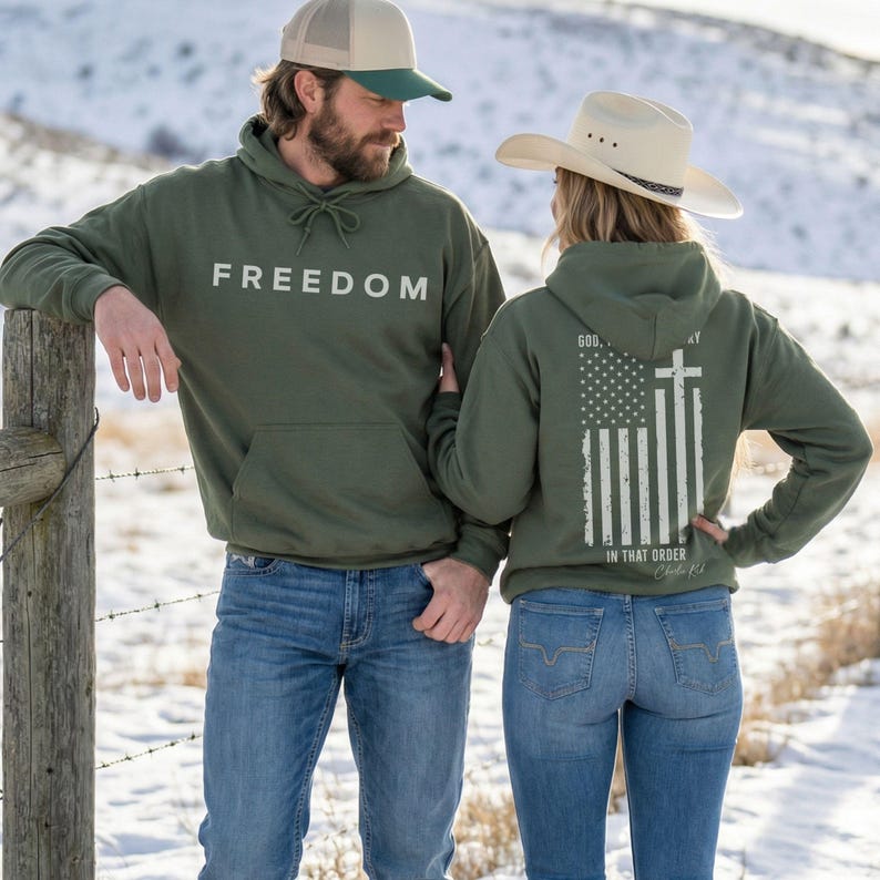 May include: Two people wearing olive green hoodies and blue jeans. The hoodie on the left has the word "FREEDOM" printed in white. The hoodie on the right features an American flag design with a cross and the text "GOD, COUNTRY, IN THAT ORDER".