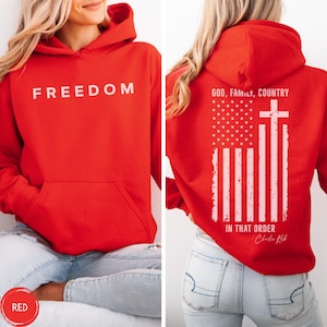 May include: Red hoodie with the word "FREEDOM" printed in white on the front. The back of the hoodie features a white graphic of the American flag with a cross and the text "GOD, FAMILY, COUNTRY IN THAT ORDER".