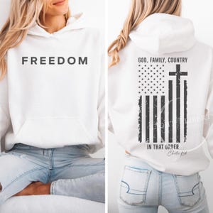 May include: White hoodie with the word "FREEDOM" printed in black on the front. The back features a distressed American flag design with a cross and the text "GOD, FAMILY, COUNTRY IN THAT ORDER".