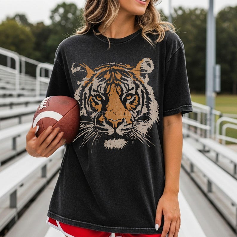 May include: A charcoal grey short-sleeve t-shirt featuring a large, detailed graphic of a tiger face in shades of orange, black, and white. The shirt has a crew neckline and a relaxed fit, showcasing a vintage-inspired, faded fabric texture.