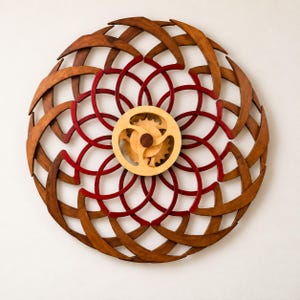 Puede incluir: Una pieza de arte mural circular con un diseño geométrico intrincado y en capas. La estructura exterior consta de segmentos curvos de madera marrón oscuro, mientras que la capa interior se compone de elementos curvos de color rojo intenso.