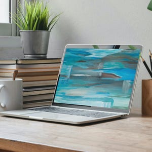 May include: A silver laptop displays an abstract painting with shades of blue, teal, and brown. The laptop sits on a wooden desk, with a stack of books, a mug, and a small potted plant in the background.