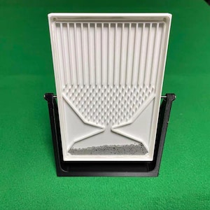 Peut inclure: Un plateau en plastique blanc avec un dessus strié et une section inférieure à motifs, soutenu par un cadre noir. Le plateau semble être conçu pour tamiser ou séparer de petites particules. Le fond est vert uni.